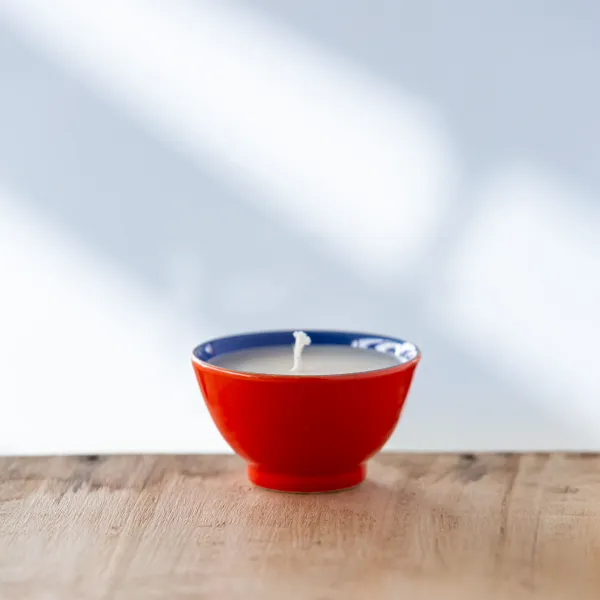 Bougie parfumée dans une tasse rouge avec bord bleu, vue de face.
